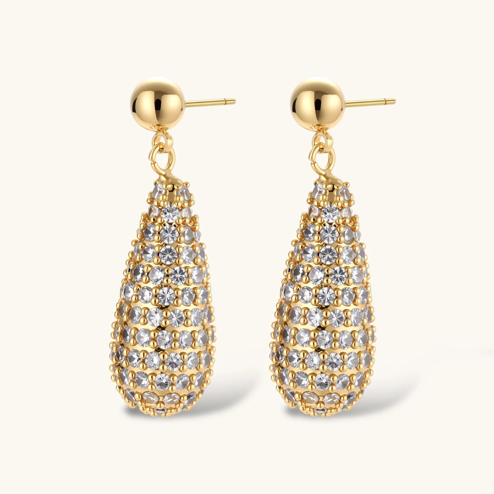 Gold-plated teardrop necklace and earrings covered in AAA cubic zirconia crystals on cream background.