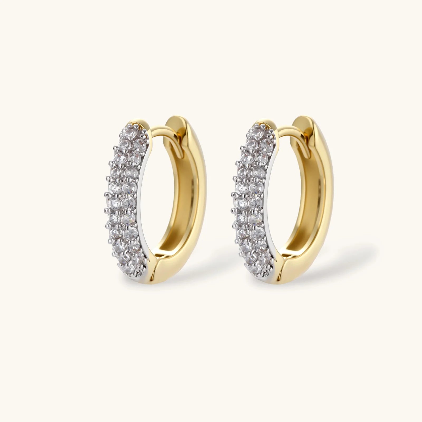 Gold-plated curved necklace, hoop earrings, and adjustable ring with pavé cubic zirconia stones on cream background.