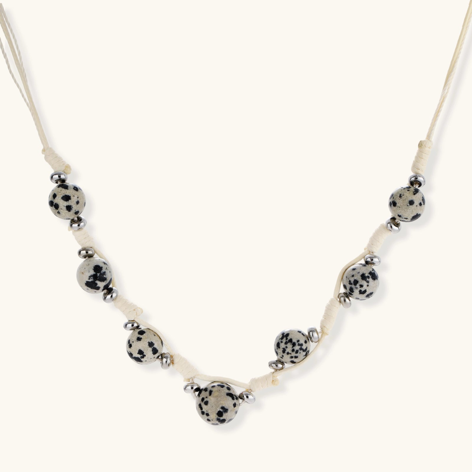 Adjustable cream cord necklace with white spotted stone beads featuring black speckles on neutral background