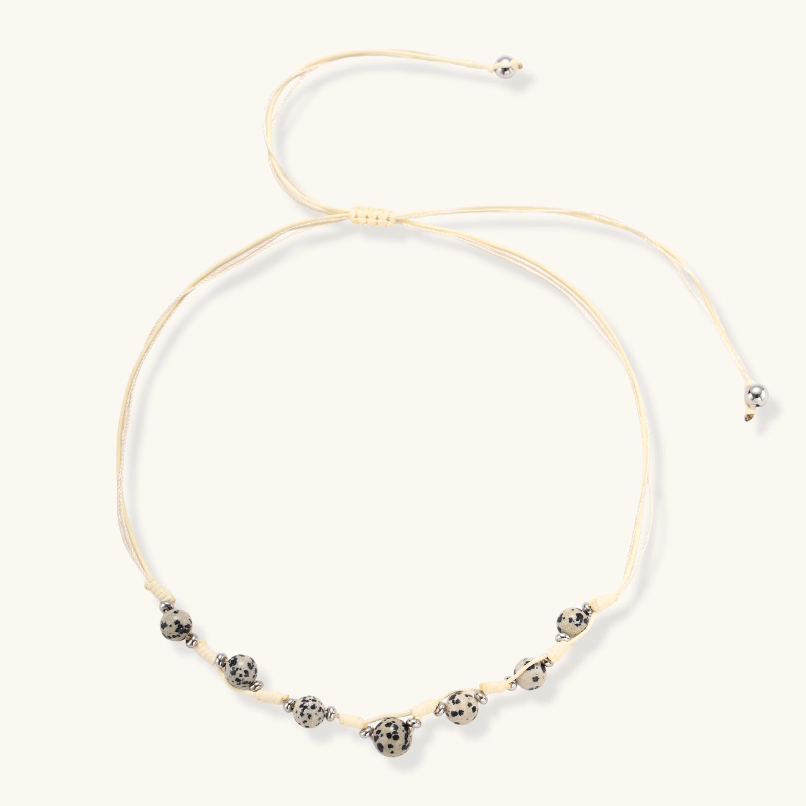 Adjustable cream cord necklace with white spotted stone beads featuring black speckles on neutral background