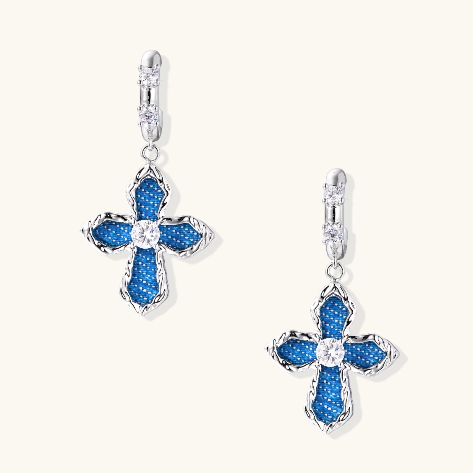 Silver hoops with denim-inlaid cross charms and clear crystals on beige background