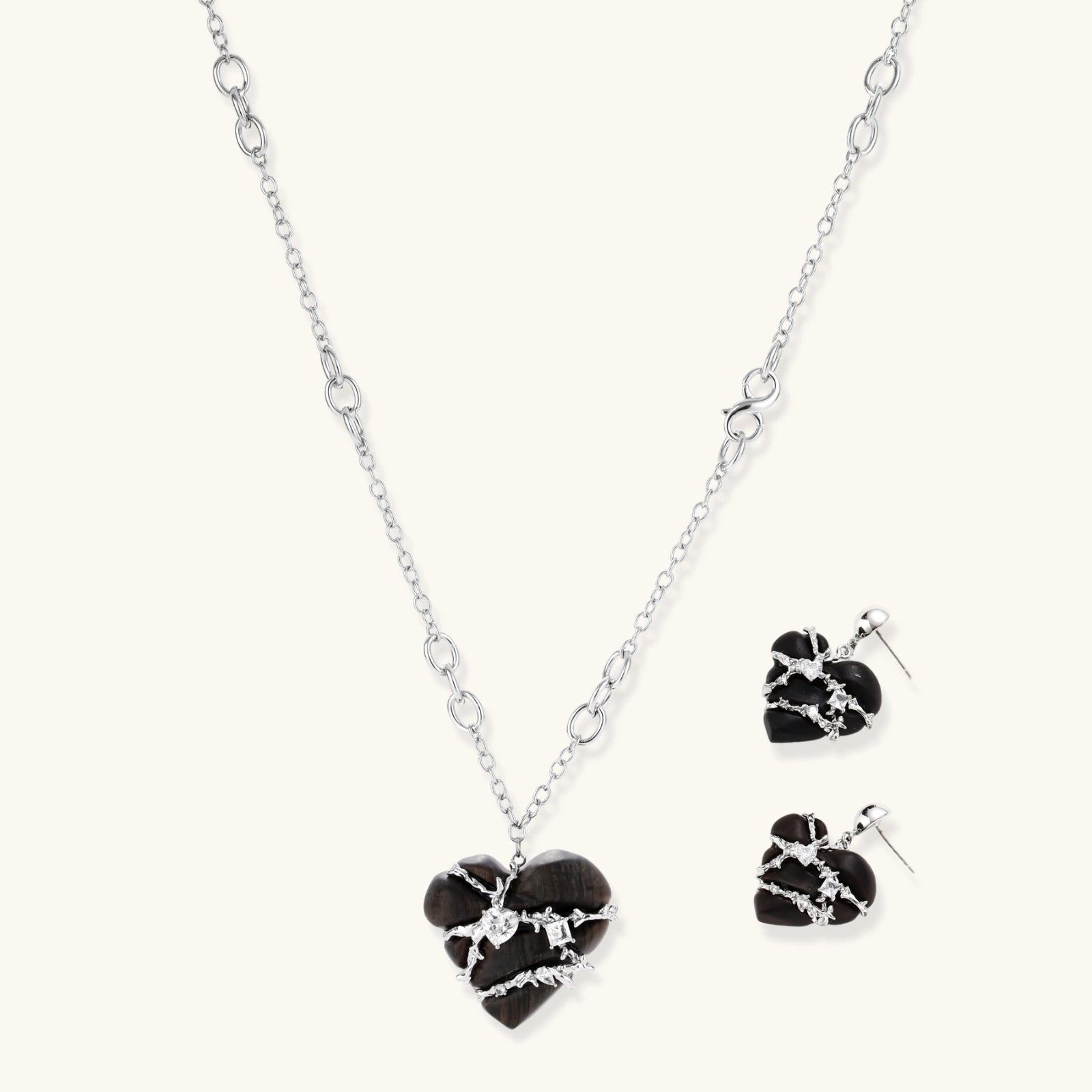 Dark ebony wood heart charms wrapped in intricate silver chains with crystal accents, shown as matching earrings and necklace set.