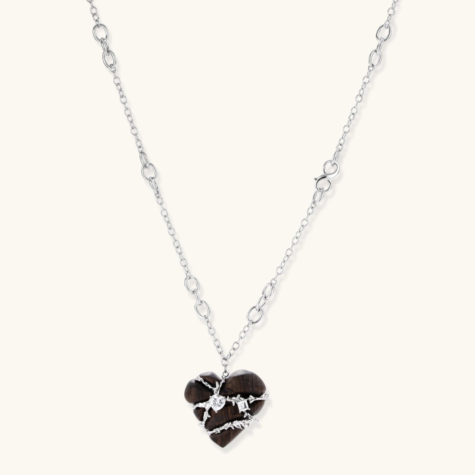 Dark ebony wood heart pendant wrapped with brass wire and zirconia crystals on adjustable chain against cream background